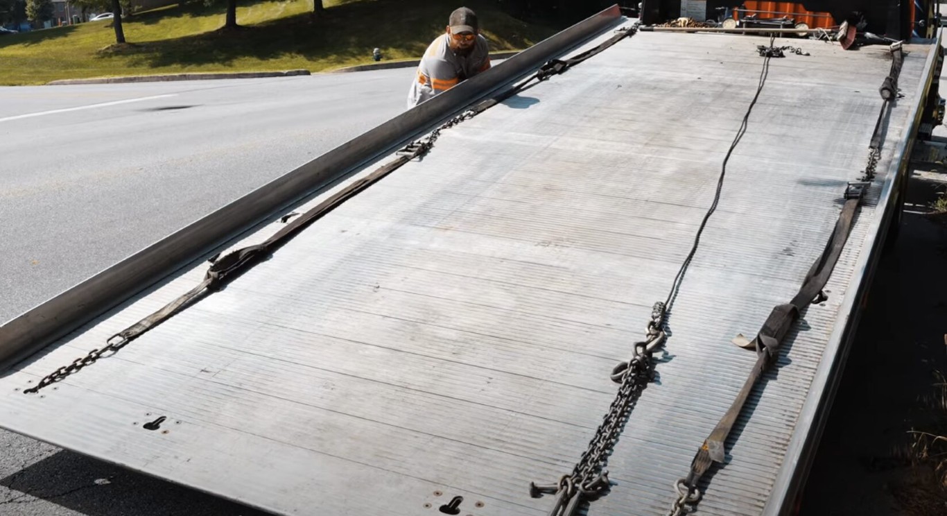 Flatbed tow truck operator securing a vehicle with chains and straps
