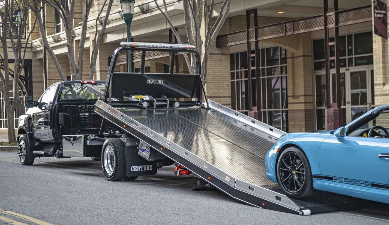 Century flatbed tow truck carefully loading a Porsche in an urban area, demonstrating professional vehicle care